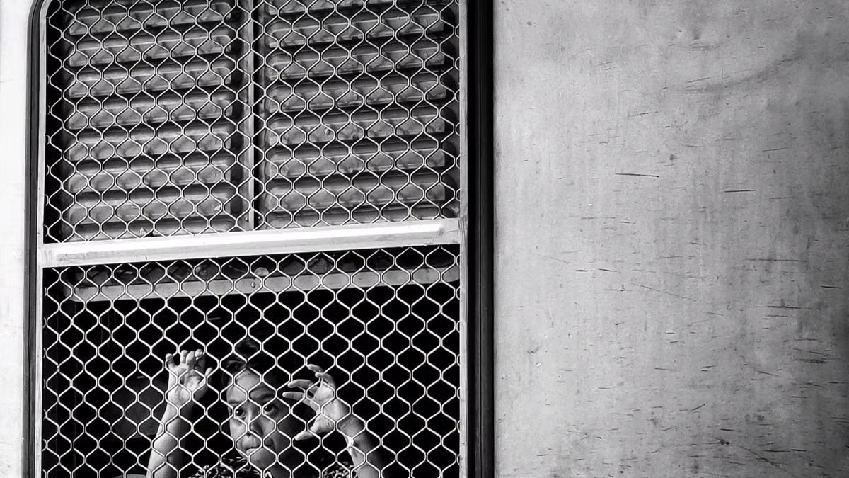 Black and white image of a child peering through a train window grate, capturing curiosity and introspection.